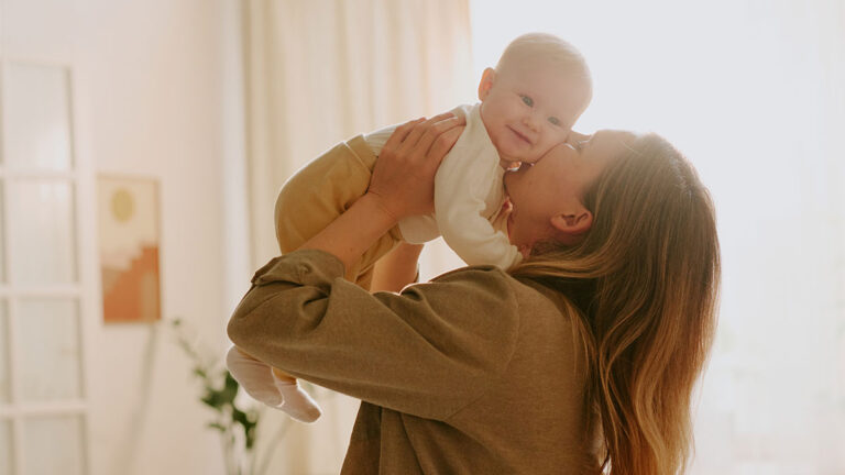 Mãe segurando e beijando seu bebê, representando o cuidado e os direitos garantidos pelo Auxílio-Maternidade.