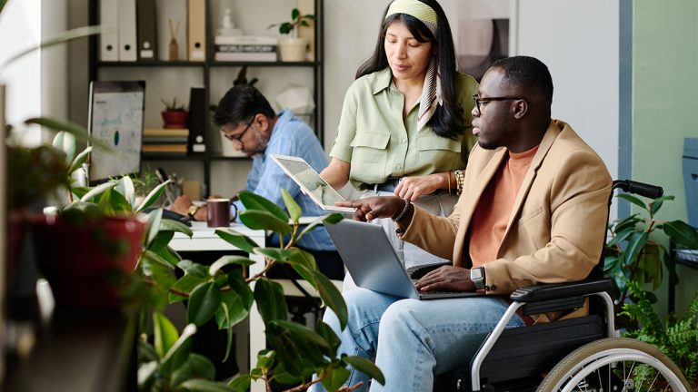 Trabalhador com deficiência conversando com colega de trabalho em escritório com plantas