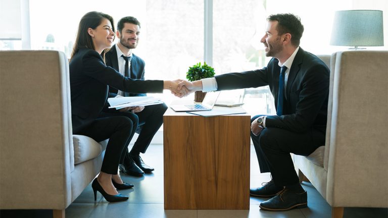 Pessoas em uma reunião de negócios em escritório moderno, com um homem e uma mulher apertando as mãos para simbolizar um acordo, representando o conceito de negociação coletiva em ambiente corporativo.