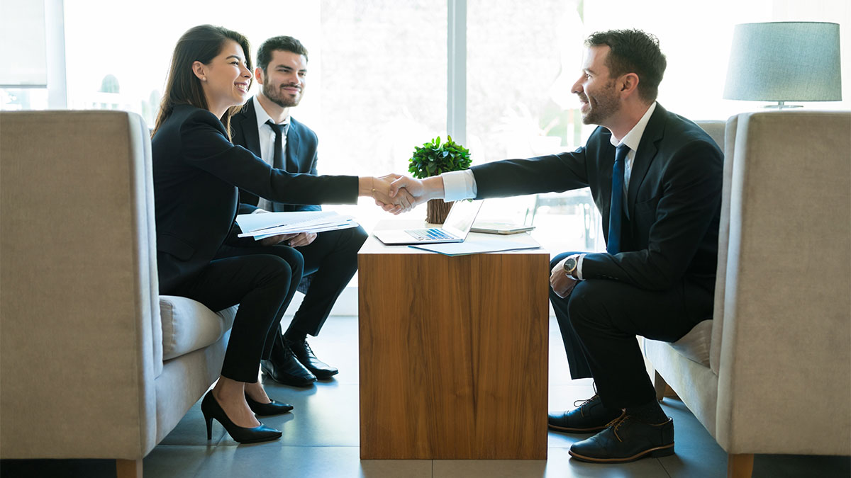 Pessoas em uma reunião de negócios em escritório moderno, com um homem e uma mulher apertando as mãos para simbolizar um acordo, representando o conceito de negociação coletiva em ambiente corporativo.