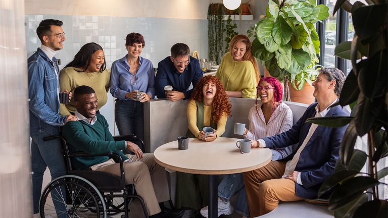 Grupo diverso de pessoas felizes reunidas em um ambiente informal, incluindo pessoa em cadeira de rodas, simbolizando diversidade inclusion equidade no ambiente de trabalho.