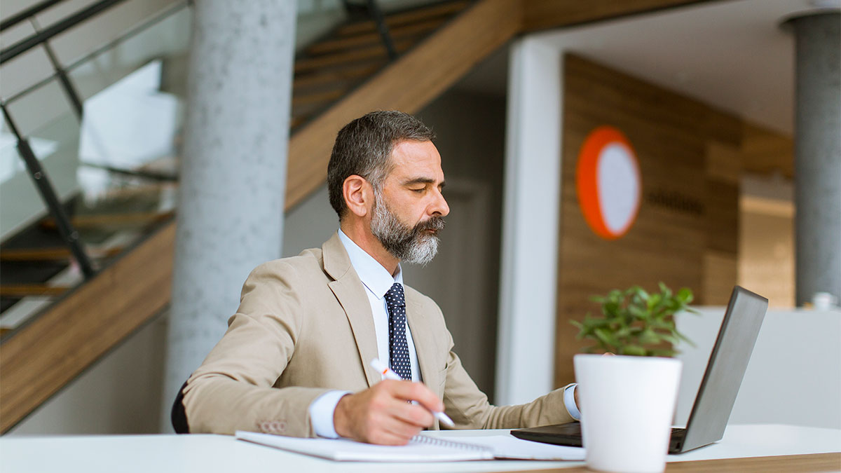 Advogado sentado em mesa olhando para o notebook analisando e identificando erros em contribuições previdenciárias para fazer a regularização.