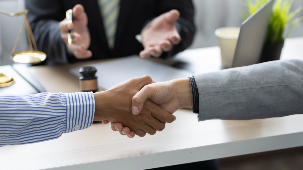 Aperto de mãos entre representantes de empresa e advogado durante negociação para prevenção de litígios trabalhistas.