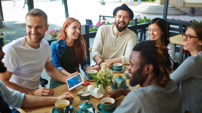 Grupo de jovens adultos conversando e rindo em uma cafeteria ao ar livre, representando momentos de descanso e convivência social fora da jornada de trabalho.