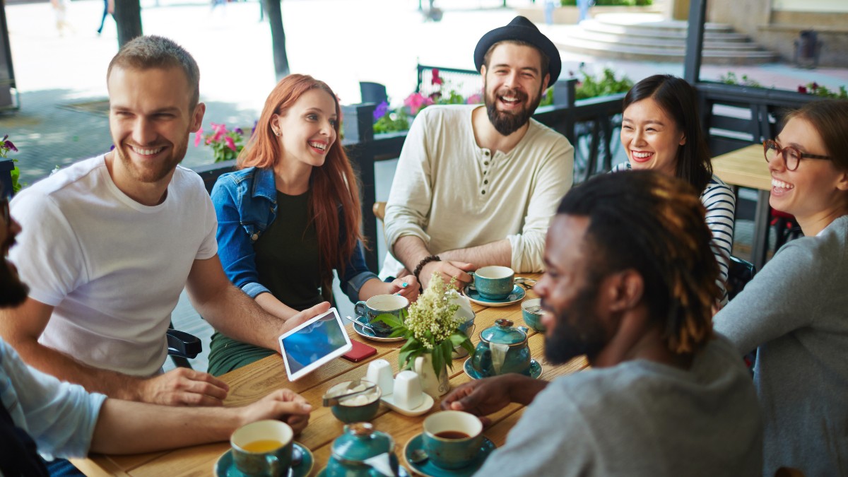 Grupo de jovens adultos conversando e rindo em uma cafeteria ao ar livre, representando momentos de descanso e convivência social fora da jornada de trabalho.